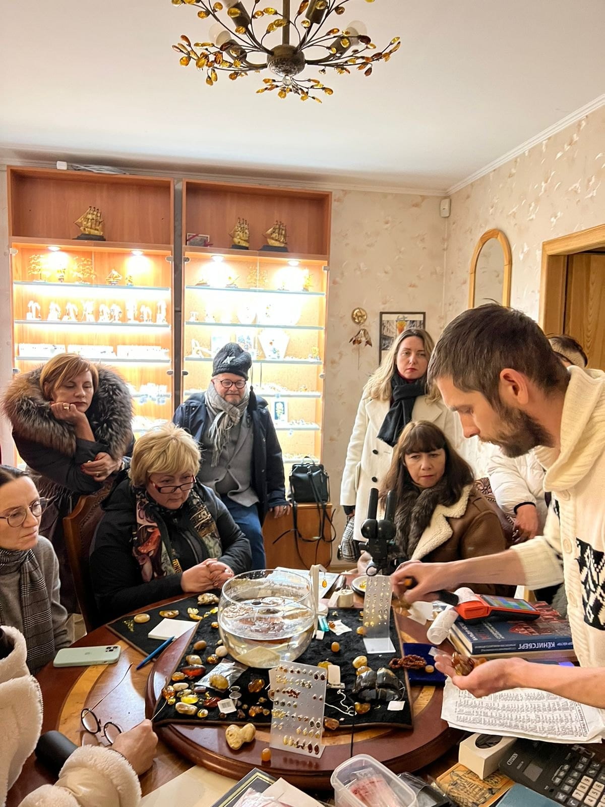 Группа посетителей за экскурсионным столом с микроскопом и образцами янтаря